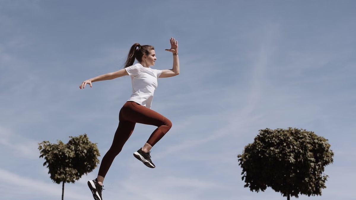 Athletic woman in action jump against a blue sky background. Captures fitness in motion.